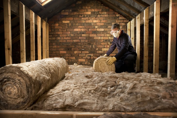 Guy laying insulation in a loft - stock image
